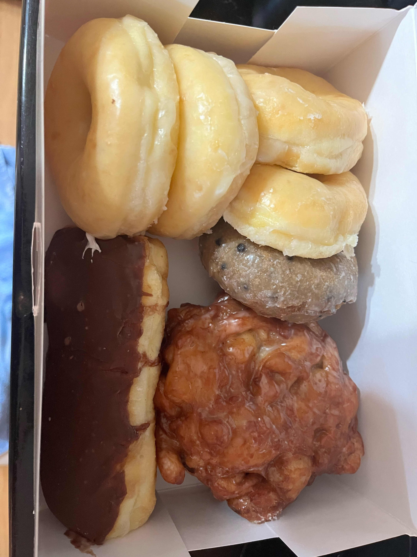 A box of glazed donuts, a chocolate long john, a blueberry cake donut and an apple fritter